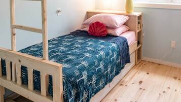 A bunk bed with a ladder, a bedside table with a lamp, a vase with a plant, and a window with a view.