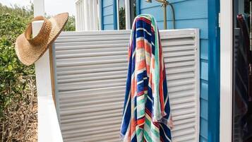 Une maison bleue avec un porche blanc, une terrasse en bois, un chapeau de paille et une serviette à rayures.