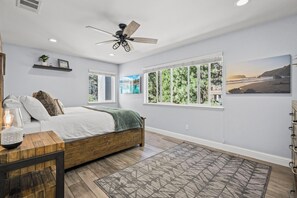 A bedroom with a bed, a ceiling fan, large windows, and a view of the outdoors.