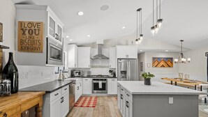 A modern kitchen with white cabinets, a central island, stainless steel appliances, and a red and white checkered rug. - Tahoe Getaway | 2 King Suites & Hot Tub | Near Town, Lake Activities & Trails (Truckee)