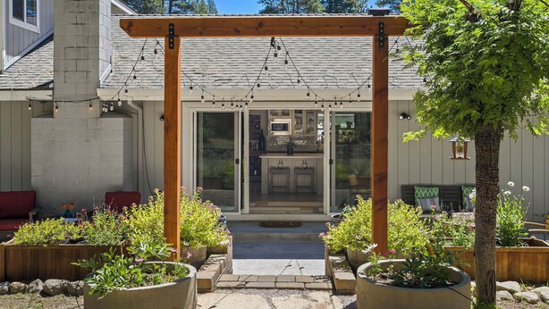 A covered outdoor area with a wooden pergola and string lights, leading to a glass door entrance. - Tahoe Getaway | 2 King Suites & Hot Tub | Near Town, Lake Activities & Trails (Truckee)