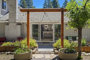 A covered outdoor area with a wooden pergola and string lights, leading to a glass door entrance. - Tahoe Getaway | 2 King Suites & Hot Tub | Near Town, Lake Activities & Trails (Truckee)