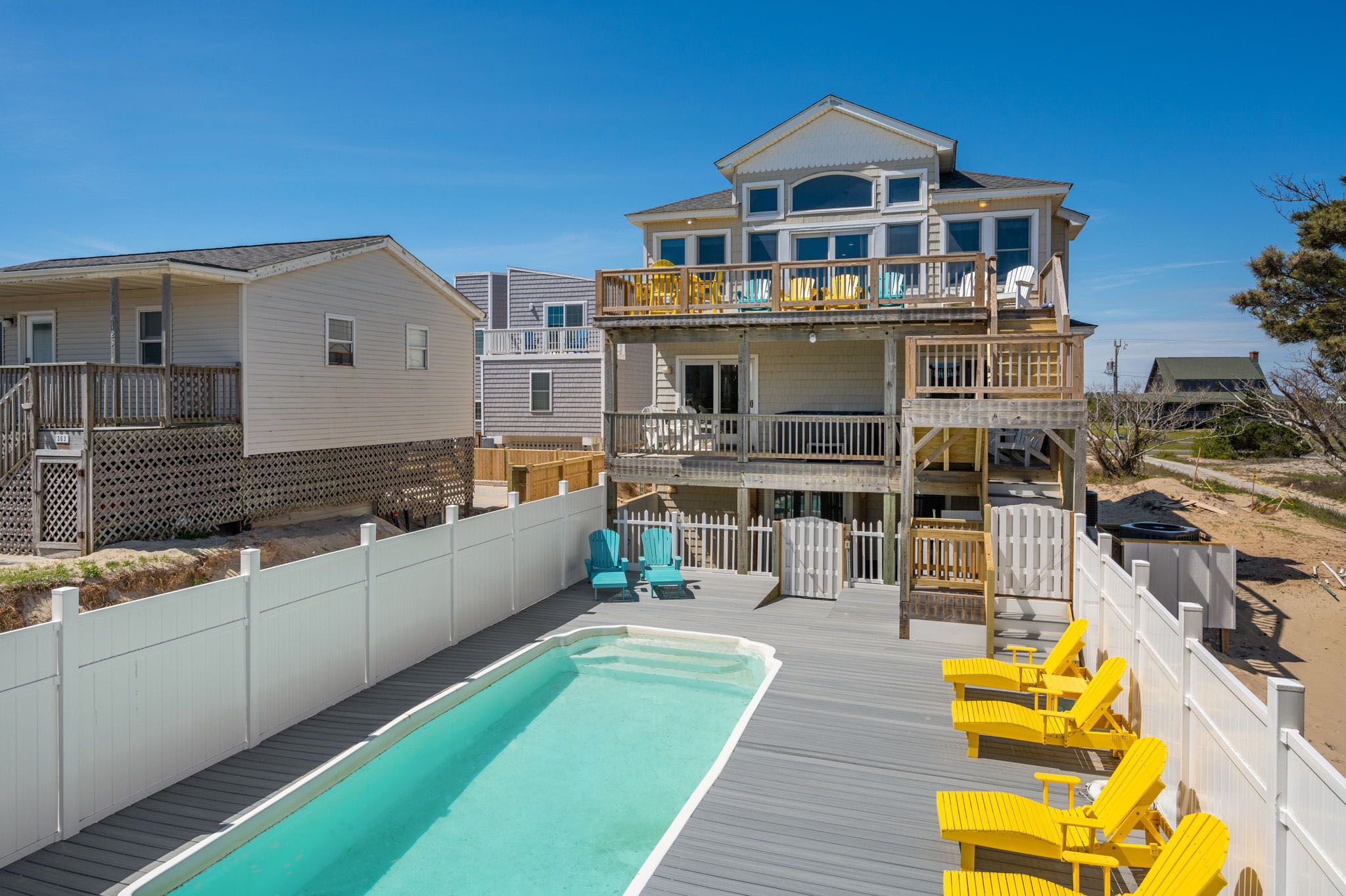 A two-story house with a pool, deck chairs, and a fenced backyard.