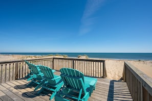 Une terrasse en bois avec des chaises turquoise donnant sur une plage.