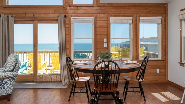 A dining area with a view of the sea, wooden walls, and a table set for four.