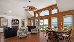A spacious living room with a fireplace, a ceiling fan, and a large window overlooking the ocean.