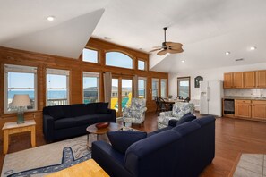 A spacious living area with a large window overlooking a scenic view, a ceiling fan, and wooden cabinetry in the adjacent kitchen.
