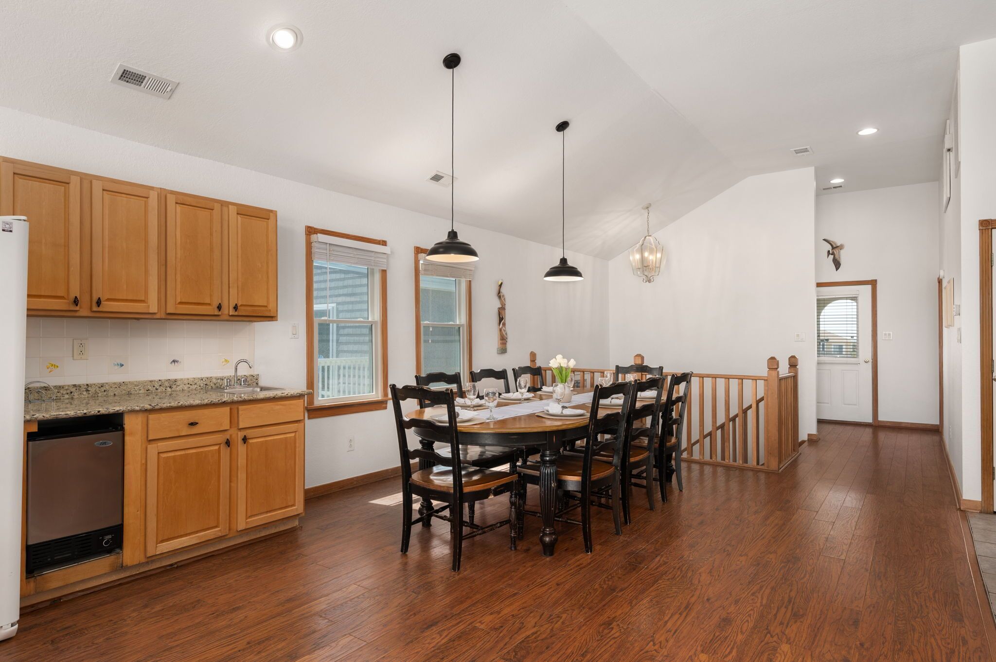 A spacious kitchen with wooden cabinets, a dining table set for six, and pendant lighting.