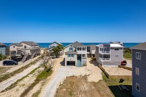 Un quartier résidentiel en bord de mer, avec des maisons, un sentier sablonneux et une vue dégagée sur l’océan.