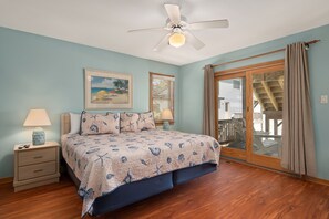 A bedroom with a bed, a nightstand, a ceiling fan, a window with blinds, and a view of a deck.