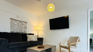 A modern living room with a dark grey sofa, a wooden coffee table, a light-colored armchair, a wall-mounted flat-screen TV, and a decorative fish wall art piece.
