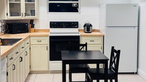 A compact kitchen with white cabinets, a black stove, a microwave, a refrigerator, and a dining table with chairs.