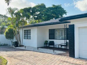 Una casa de un piso con fachada blanca, techo negro y entrada de adoquines.