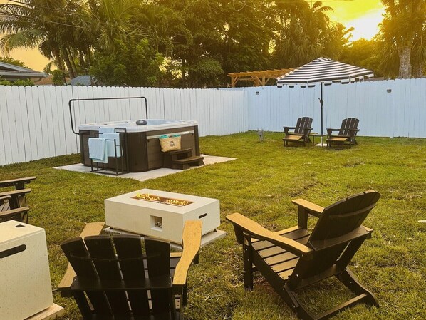 A backyard with a hot tub, outdoor seating, and a fire pit.