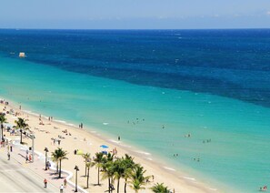 Una playa con aguas turquesas cristalinas, palmeras y gente disfrutando del sol y el mar.