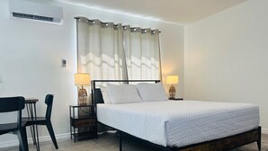 A bedroom with a bed, two bedside tables with lamps, a chair, and a window with curtains.
