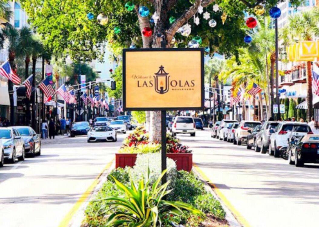 A street view with a sign for 'Las Olas' hotel, surrounded by parked cars and palm trees.