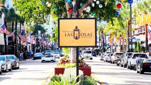 Straatbeeld met een bord voor hotel 'Las Olas', omringd door geparkeerde auto's en palmbomen.