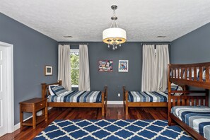 Une chambre avec deux lits simples, un lit superposé, une table de chevet en bois, un tapis à motifs et un lustre.