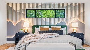A bedroom with a bed, two bedside tables, a large window, and a wall with vertical lines. - Symphony of Luxury|Hot Tub+Game Room+Sauna+Views (Leicester)