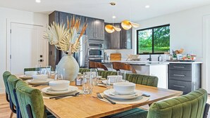 A modern kitchen with dark cabinets, a wooden dining table, and green upholstered chairs. - Symphony of Luxury|Hot Tub+Game Room+Sauna+Views (Leicester)