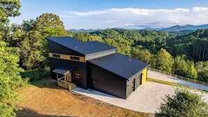 A modern house with a large garage and a covered patio area, surrounded by a forested landscape. - Symphony of Luxury|Hot Tub+Game Room+Sauna+Views (Leicester)