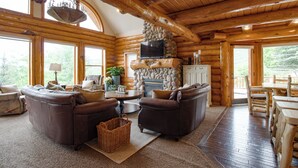 Ein rustikaler Innenraum einer Blockhütte mit Ledersofas, einem Kamin aus Stein und einem Essbereich.