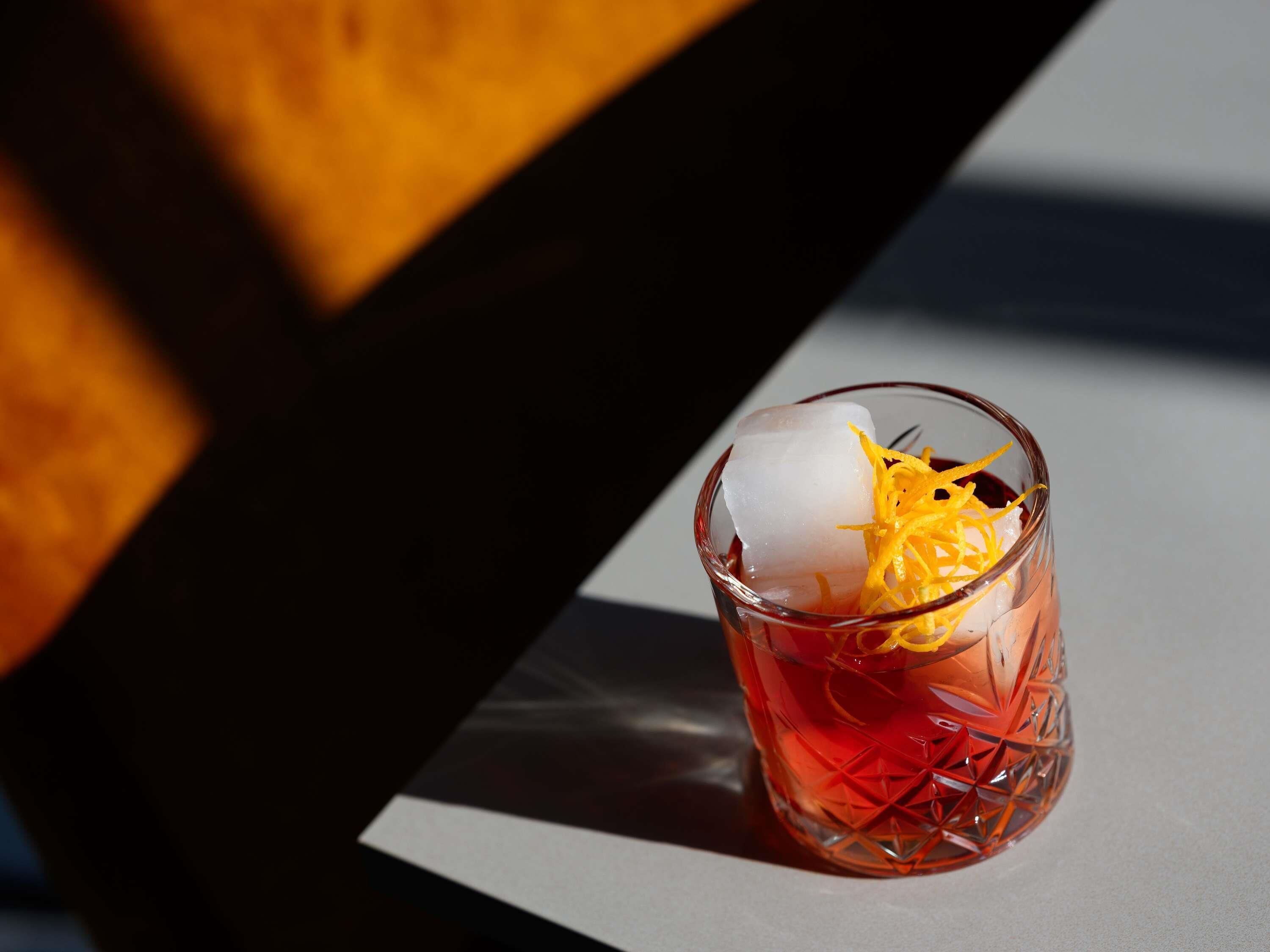 A glass with ice cubes and orange peel garnish on a table.