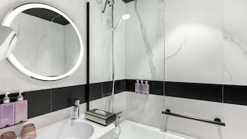 Un bagno moderno con un lavandino bianco, uno specchio rotondo, un soffione doccia a mano e una doccetta.