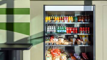 A vending machine stocked with beverages and snacks, located in a modern interior with geometric wall patterns and a tiled floor.
