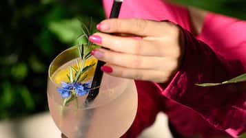 Una persona sosteniendo una copa de cóctel con una pajita, que contiene una flor azul y una ramita de romero.