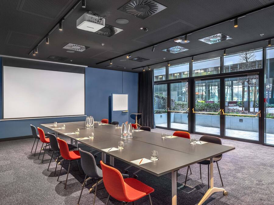 Un salón de conferencias con una mesa grande, sillas, un proyector y una pizarra.
