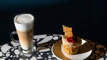 Una taza de café con espuma y un postre pequeño sobre un plato con forro de papel, sobre una mesa con vetas.