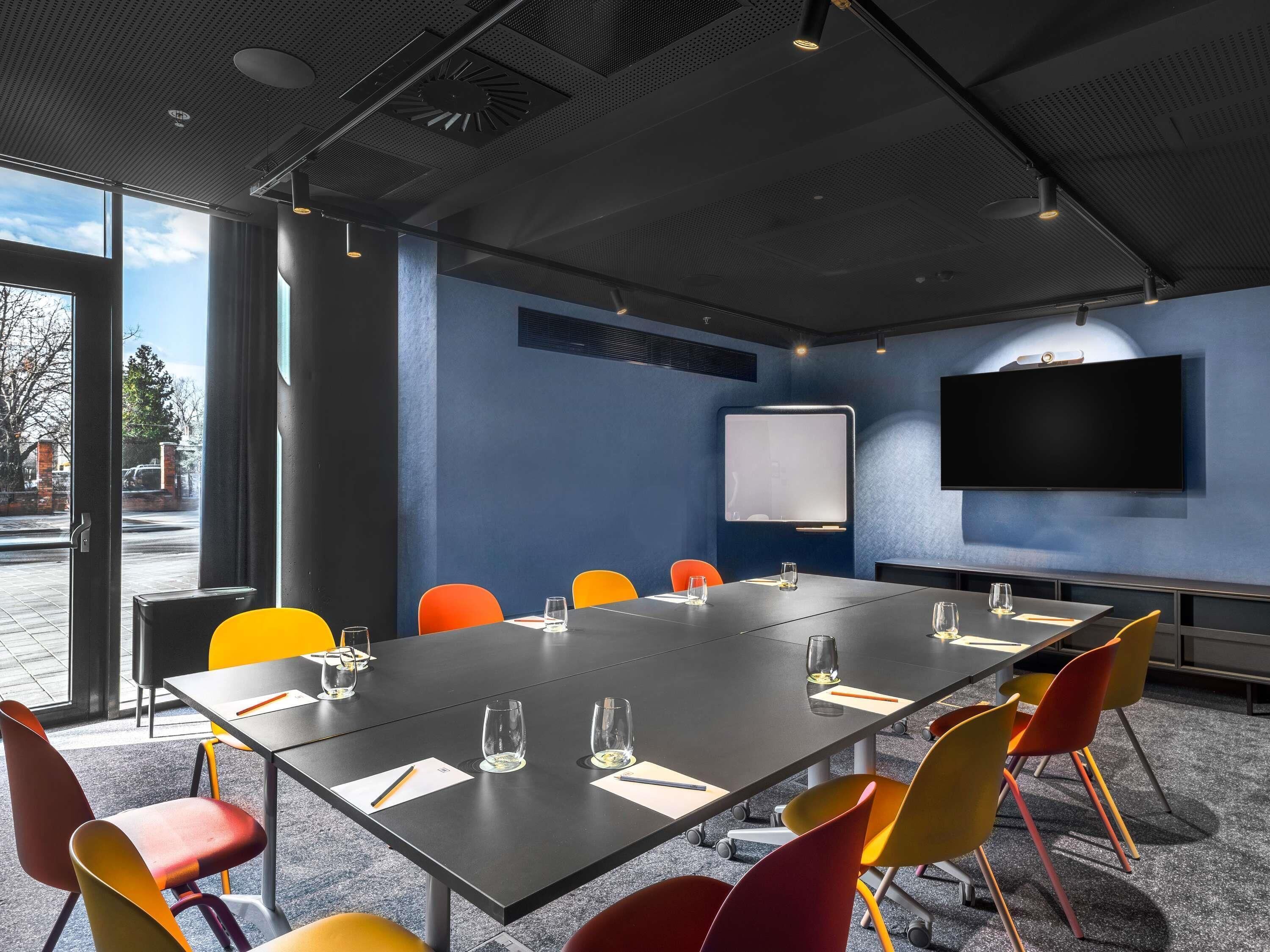 A conference room with a long table, colorful chairs, a whiteboard, and a TV on the wall.
