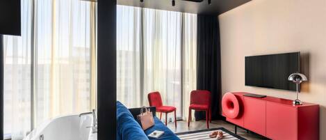 Una sala de estar moderna con un ventanal grande, un televisor de pantalla plana, un mueble rojo y un sofá azul.