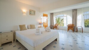Une chambre d’hôtel avec un grand lit, deux tables de chevet, une chaise, une table et une fenêtre avec des rideaux.