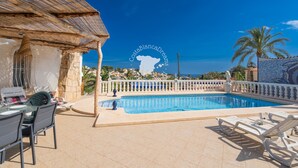 Une piscine entourée d’une clôture blanche, avec des chaises longues et une table avec des chaises.