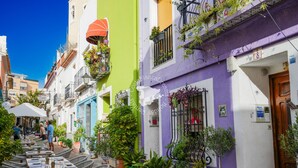 Une rue étroite avec des tables en terrasse et des plantes en pot.