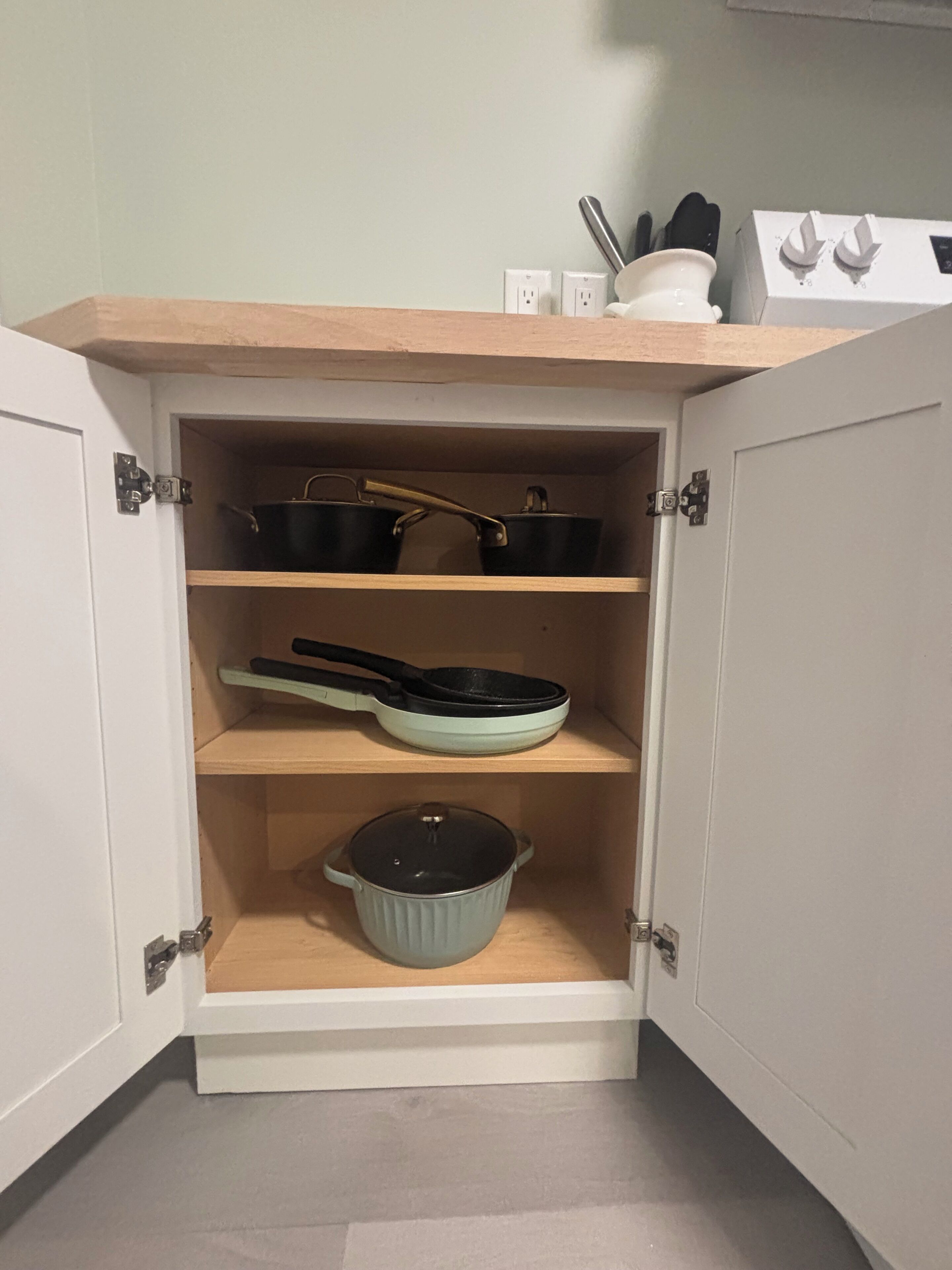 Un meuble de cuisine avec trois étagères : une casserole sur l’étagère du bas, une poêle sur l’étagère du milieu et une autre casserole sur l’étagère du haut.