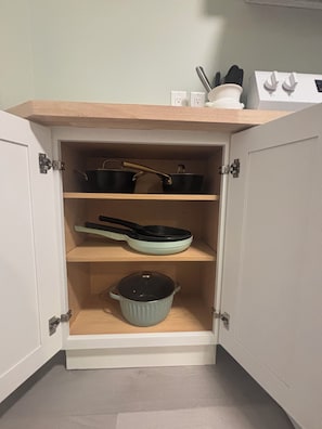 Un meuble de cuisine avec trois étagères : une casserole sur l’étagère du bas, une poêle sur l’étagère du milieu et une autre casserole sur l’étagère du haut.