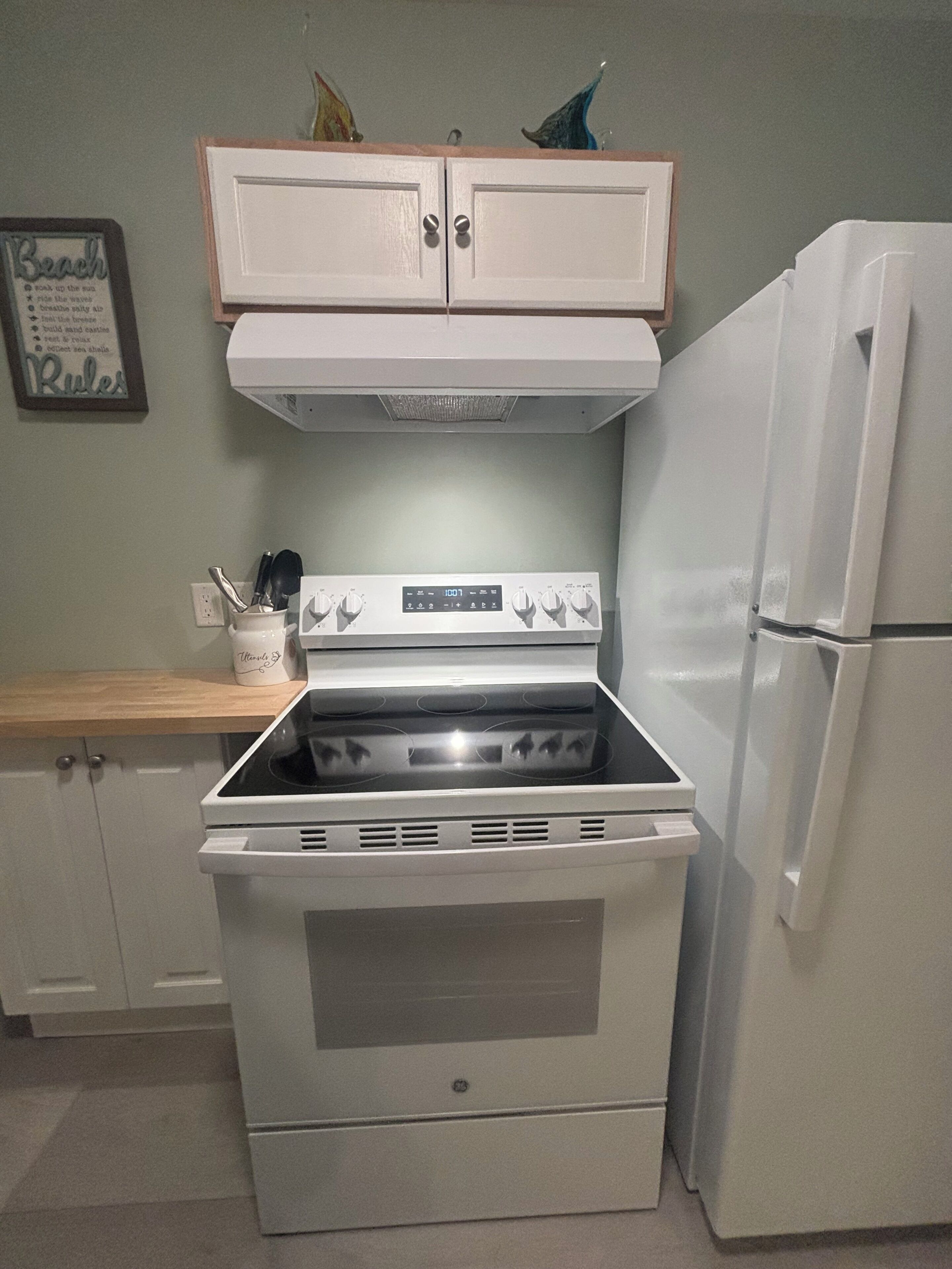 A kitchen with a white stove, a white refrigerator, and a wooden cabinet above the stove.