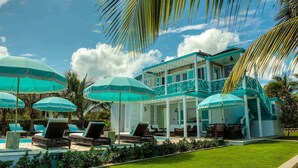 A two-story house with a balcony, a pool area with lounge chairs, and multiple umbrellas. - Charming waterfront Caribbean estate - 2 min from pink sand beach (Little Harbour)