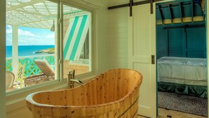 A room with a wooden bathtub, a bed, and a view of the ocean. - Charming waterfront Caribbean estate - 2 min from pink sand beach (Little Harbour)