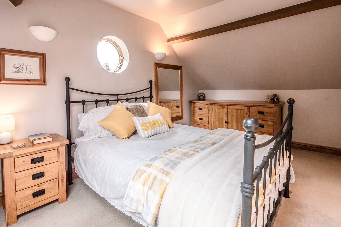 Een slaapkamer met een bed, nachtkastjes, een houten dressoir, een spiegel en een plafondlamp.
