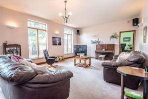 A spacious living room with leather sofas, a wooden coffee table, a television, and a bookshelf.