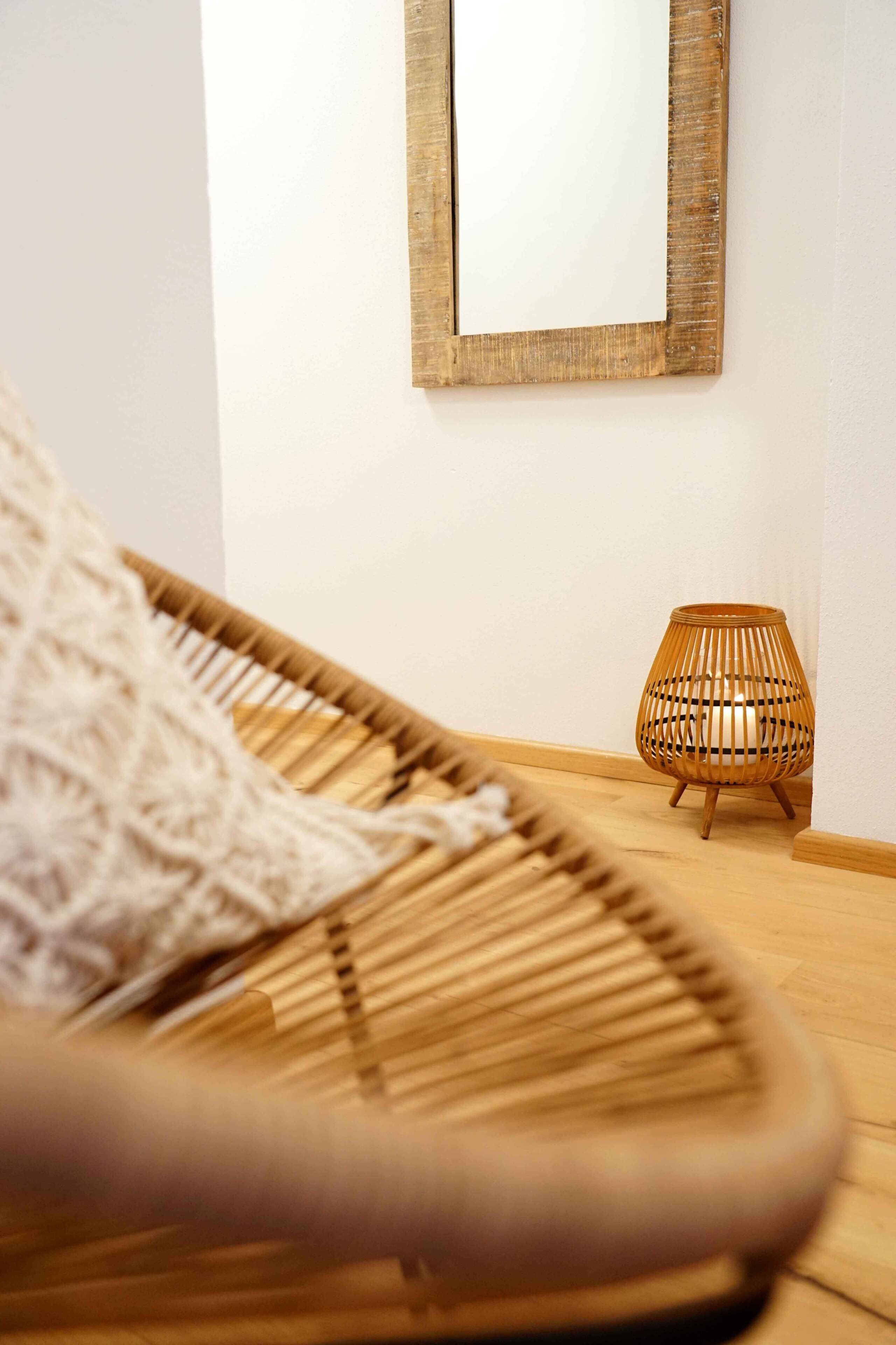 Ein Korbstuhl mit weißer Decke, Holzboden und ein kleiner Holztisch mit einer gewobenen Lampe.