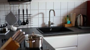 A modern kitchen with a black sink, white cabinets, and a stainless steel kettle. - Sun II für 1-4 Personen, 60 m², Schlafzimmer, Wohn/schlafzimmer, Küche, Bad, Balkon, Wlan (Marquartstein)