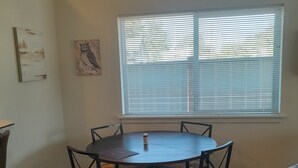 Una mesa redonda para comer con seis sillas, una ventana con persianas y un cuadro de un búho colgado en la pared.