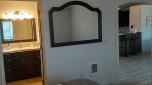 Un dormitorio con cama, un espejo grande y una kitchenette al fondo.