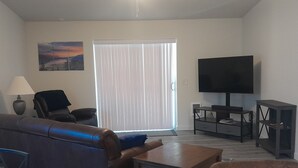 Una sala de estar con ventilador de techo, televisor de pantalla plana, sofá, mesa de centro y un cuadro en la pared.
